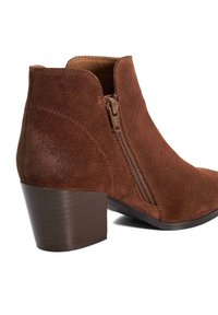 Bottine en suede marron avec une finition texturée, fermeture éclair sur le côté et un petit talon empilé. Le design présente une pointe arrondie et des bords sans coutures.
