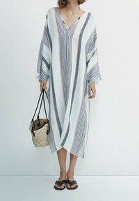 Robe oversize à rayures avec un col en V en bleu clair et bleu foncé, en tissu texturé. Assortie à un sac tressé et des sandales noires.