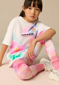 Maglietta bianca oversize con un colorato motivo tie-dye pastello e testo stampato, abbinata a leggings attillati multicolori e calzini alla caviglia rosa.