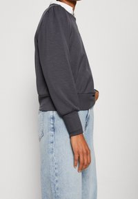 Grijze sweatshirt met lange mouwen, ronde hals, elastische boorden en een aansluitende onderrand, gecombineerd met lichtblauwe, losse jeans. Eenvoudig ontwerp.