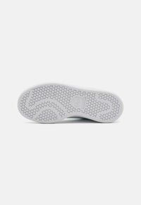 White sneaker sole with a patterned tread, featuring hexagonal indents and an embossed logo. Smooth rubber material, rounded shape.