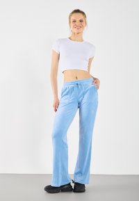 Lyseblå velour joggebukser med strikk i livet, vide ben og to frontlommer, sammen med en hvit cropped T-skjorte.