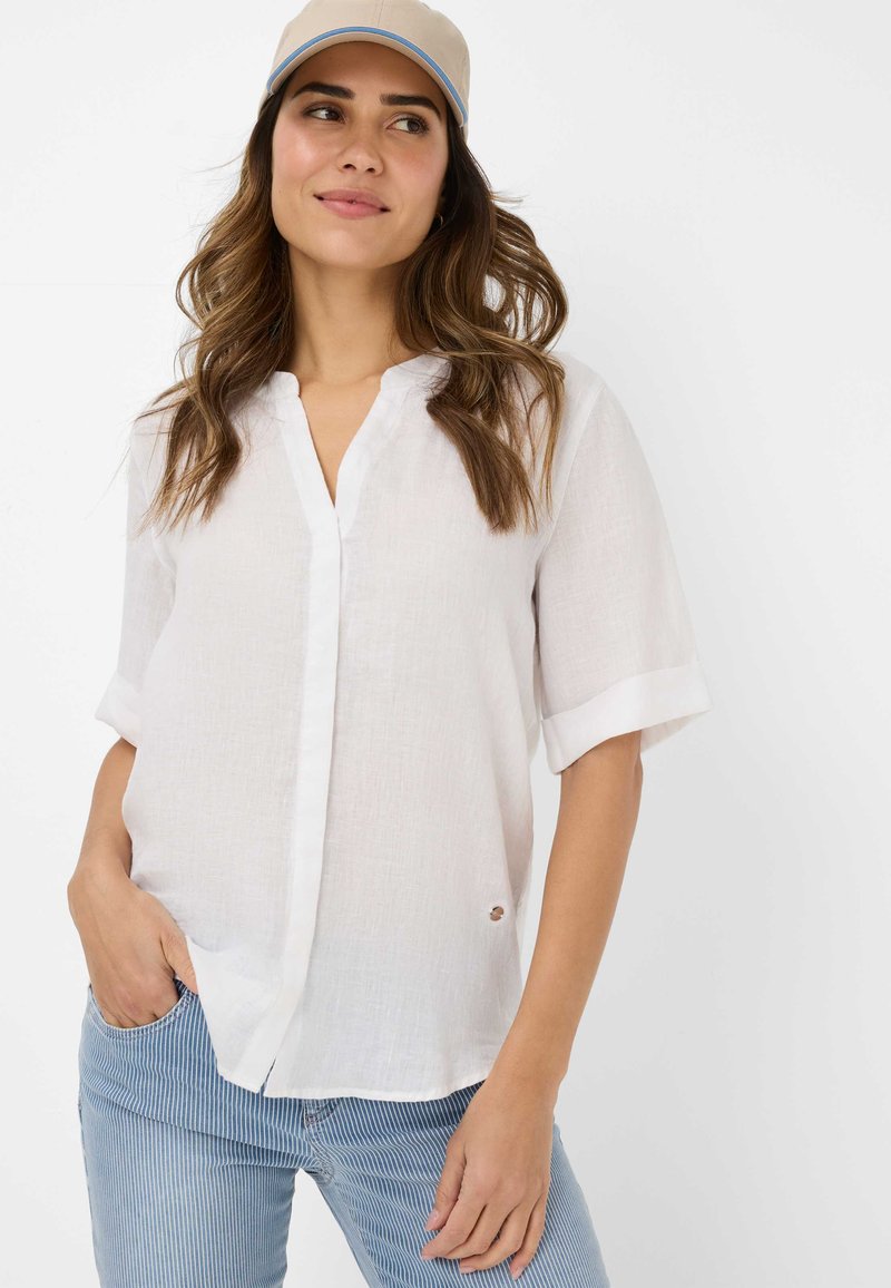 Witte linnen shirt met een knoopsluiting aan de voorkant, korte opgerolde mouwen en een klein rond detail aan de onderkant, gecombineerd met blauw gestreepte broek.