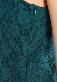 Türkisfarbenes Spitzenkleid mit Blumenmustern und strukturiertem Finish, mit einem verdeckten Reißverschluss auf der Rückseite und einer figurbetonten Silhouette.