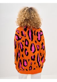 Oversized orange sweater featuring a bold black and pink leopard print, with ribbed cuffs and hem. Smooth knit texture and relaxed fit.