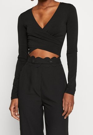 Crop top noir à manches longues avec un col en V et un design croisé, associé à un pantalon taille haute avec une ceinture festonnée et deux boutons.