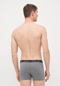 Graue Baumwollboxershorts mit schwarzem Bund, der den Text "PIER ONE" zeigt, dargestellt aus der Rückansicht des Models. Glattes Material, taillierte Passform.