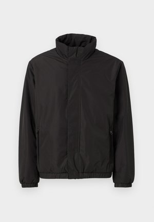 Giacca nera impermeabile con colletto alto, tasche laterali con zip, polsini elasticizzati e vita aderente. Tessuto in poliestere liscio e opaco.