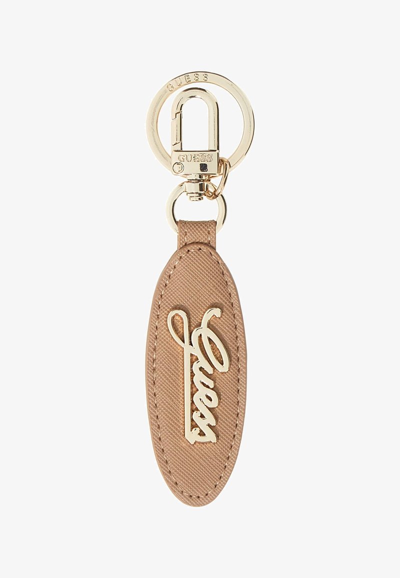 Porte-clés avec une étiquette en tissu beige doux portant un logo "Guess" en métal doré. Attaché à un anneau circulaire doré et un matériel de verrouillage.