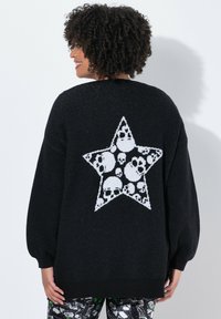 Pull noir avec une grande étoile blanche ornée de motifs de crânes au dos. Texture douce et manches amples en forme de ballon.