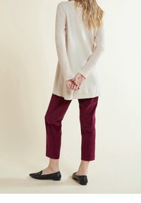 Beige knit long-sleeve tunic with ribbed texture, paired with burgundy corduroy pants and black flat shoes, viewed from the back.