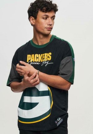 T-shirt noir avec des accents verts et gris, affichant le texte "PACKERS Green Bay" et un grand logo stylisé. Manches courtes, coupe décontractée.