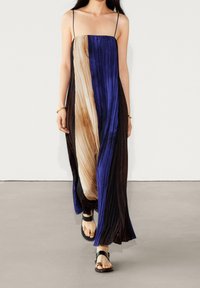 Maxikleid mit Falten und dünnen Trägern, ausgestattet mit blauen, braunen und schwarzen Farbakzenten. Glattes Gewebe mit fließender Silhouette. Getragen mit schwarzen Sandalen.