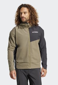 Olijfgroene en zwarte zip-up jas met capuchon, voorzien van een TERREX-logo, een soepele textuur en een contrasterend paneelontwerp.