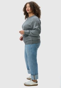 Felpa grigia a pois con polsini e orlo a coste, abbinata a jeans azzurri con risvolto e sneakers bianche con dettagli grigi.