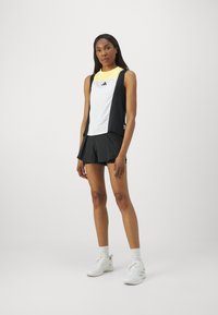 Sportoutfit bestehend aus einem ärmellosen Oberteil in Weiß und Schwarz mit gelben Akzenten und einer schwarzen Shorts. Leichter Stoff und sportliches Design.