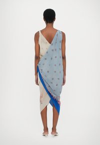 Robe en soie multicolore avec motifs floraux, design drapé et accents bleus asymétriques, dos nu et détail noué.