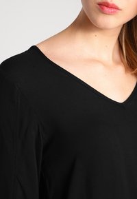Czarny top w serek, wykonany z miękkiego materiału, charakteryzujący się gładką fakturą oraz delikatnym wykończeniem przy dekolcie i szwach na ramionach.