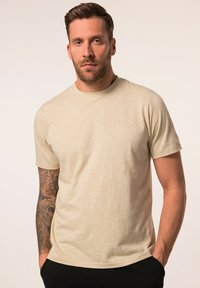 Camiseta de manga corta color crema en una tela ligera y suave con una textura sutil; presenta un escote redondo y un pequeño logo en el pecho.