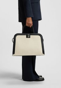 Borsa a mano in canvas beige con rifiniture e manici in pelle nera, design strutturato e meccanismo di chiusura sicuro.