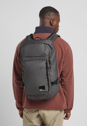 Grijze stoffen rugzak met gevoerde schouderbanden, meerdere ritscompartimenten en een zwart logo. Draag je over een bordeauxrode fleece jack.