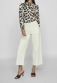 Blouse à imprimé léopard avec un col froncé, associée à un pantalon crème taille haute à jambes larges et des chaussures marron à brides.