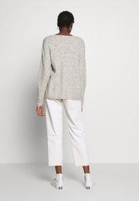 Pull en tricot gris à coupe ample et à encolure large, associé à un pantalon court blanc et des chaussures blanches. Design minimaliste et texture évidente.