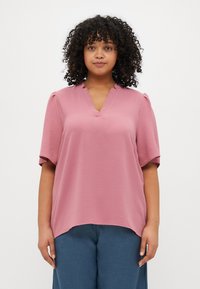Pink short-sleeve blouse with a V-neck and subtle texture, paired with loose blue trousers. Hemline is curved at the bottom.