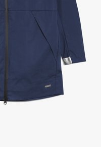 Granatowa wodoodporna kurtka z zamkiem z przodu, boczną kieszenią i srebrnymi akcentami na mankietach. Gładka tekstura i minimalistyczny design.