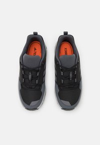 Baskets noires de sport avec une tige en maille, des accents gris et une semelle intérieure orange. Présentent un design à lacets et une semelle texturée pour l'adhérence.