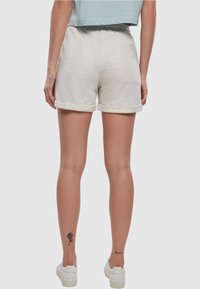 Lys grå, myke stoffshorts med rullekant, elastisk midje og baklomme. Kombinert med hvite sneakers.