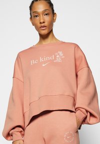 Sweatshirt rosa com ombros caídos, punhos canelados e bainha cropped. Apresenta o texto "Seja gentil" e um gráfico floral em branco.