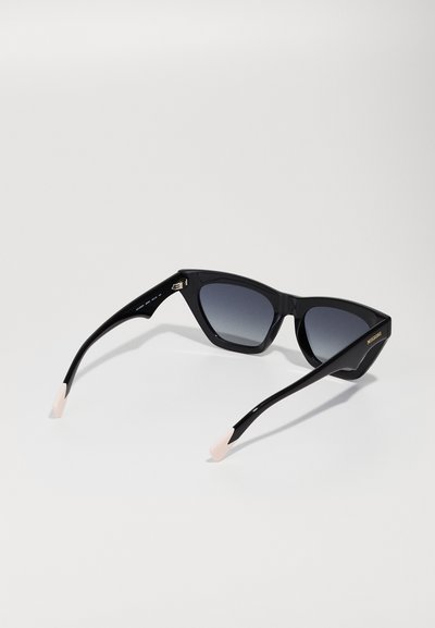 Óculos de sol pretos com uma forma acentuada de olhos de gato, lentes degradê, acabamento brilhante na armação e pontas em pastel nas hastes. Logo da marca em dourado na lateral.