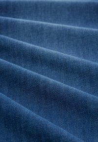 Tmavě modrá džínovina jemně se skládá s hladkou texturou, s jemnými odstíny a detailním jemným tkaním po celé ploše.