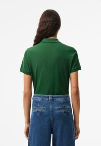Polo vert avec un col classique, des manches courtes et un tissu lisse, associé à un pantalon en denim bleu. Présente des détails de marque subtils.
