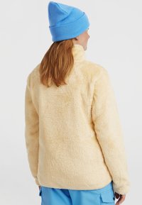 Fleece jack in zacht beige, met een hoge kraag en lange mouwen. Gecombineerd met een lichtblauwe beanie, gestyled voor comfort en warmte.