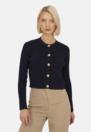 Cardigan a coste navy con maniche lunghe, caratterizzato da bottoni dorati e due piccole tasche frontali. Design cropped, realizzato in tessuto morbido.