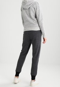 Felpa grigia con lavorazione a maglia e cappuccio regolabile, abbinata a pantaloni jogger grigi scuri con polsi neri a costine e scarpe bianche.