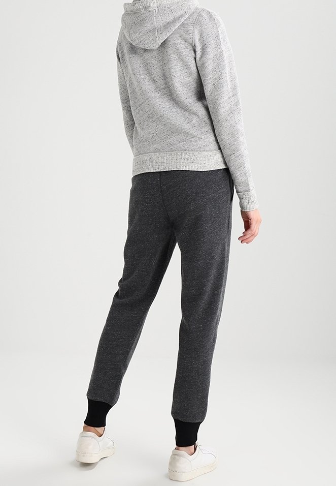 Felpa grigia con lavorazione a maglia e cappuccio regolabile, abbinata a pantaloni jogger grigi scuri con polsi neri a costine e scarpe bianche.