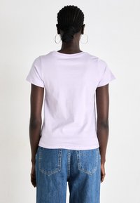 T-shirt à manches courtes lavande en coton, avec un col rond et une silhouette ajustée, présenté de dos avec un jean bleu.