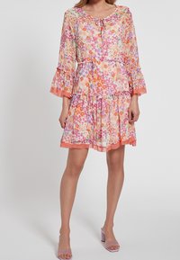 Květinové šaty vyrobené z lehkého materiálu, které obsahují barvy jako růžová, oranžová a zelená. Mají volánková ramena a sukni ve vrstveném stylu s zavazováním na krku.