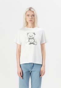 T-shirt en coton blanc avec un graphique de ours en peluche en noir et blanc. Manches courtes et coupe décontractée, associé à un jean bleu clair.