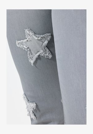 Grå denim bukser med slidte stjernelapper på knæene. Stoffet har en glat tekstur med en let stræk.