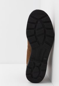 Bota de ante marrón con suela de goma negra, que presenta un patrón de tracción para un mejor agarre y una marca en relieve en el costado de la suela.