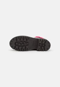 Semelle extérieure en caoutchouc noir avec des crampons profonds et une bordure en fourrure rose visible sur le bord d'une botte d'hiver sur fond blanc.