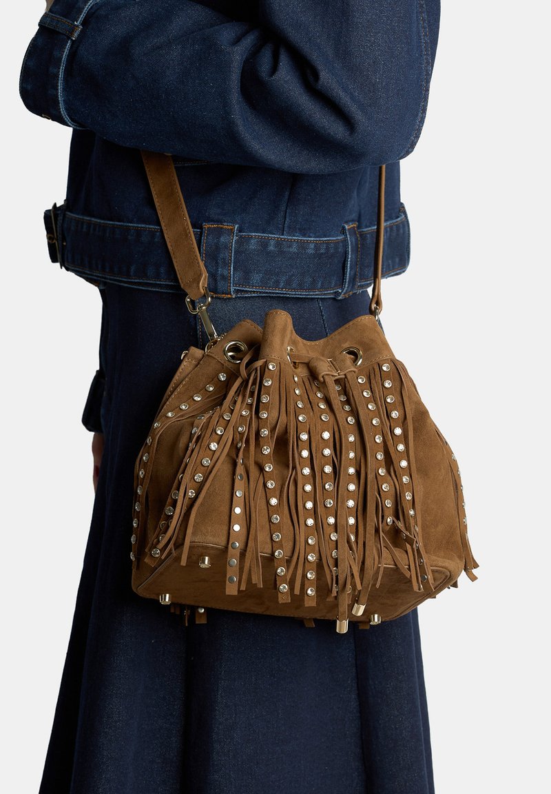 Borsa a secchiello in camoscio marrone con frange e borchie argentate, dotata di chiusura con coulisse e tracolla removibile.