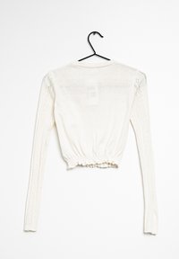 White knitted long-sleeve cropped sweater with ruched hem, hanging on black hanger against white background.