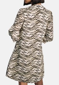 Kurzärmliges, knielanges Kleid in Creme mit einem schwarzen und braunen Tigerstreifenmuster. Verfügt über Puffärmel und eine gerade Silhouette.