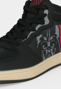 Μαύρο sneaker υψηλής κορυφής με μαύρα κορδόνια, μπεζ σόλα και γκρι και κόκκινο γραφικό με το κράνος του Darth Vader στο πλαϊνό πάνελ.