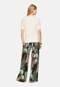 White short-sleeve top with a round neck, paired with wide-leg black trousers featuring colorful tropical leaf patterns.